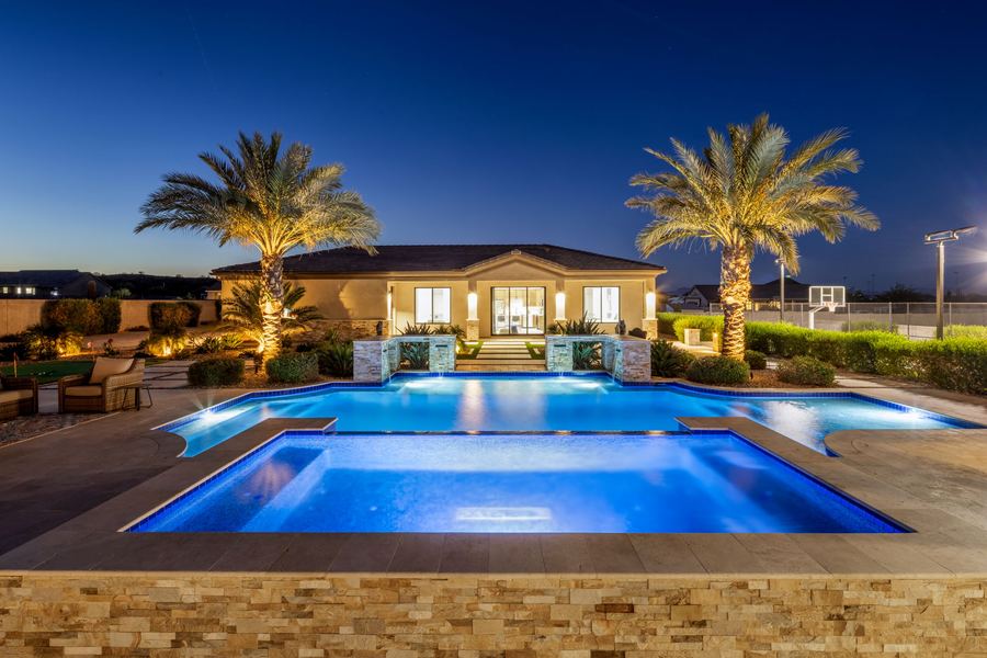 Lit pool and raised spa at blue hour with palms framing the pool house
