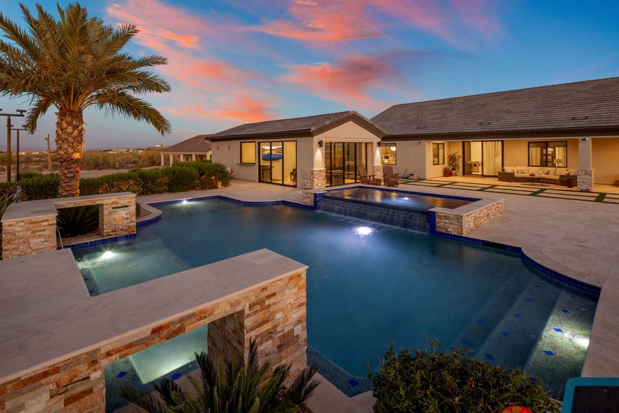 Lit pool at dusk with stacked stone pillars and the main house beyond