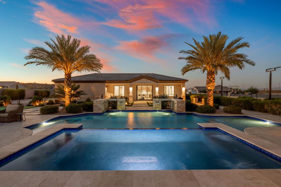Pool with sun shelf facing the pool house under a pink sunset sky