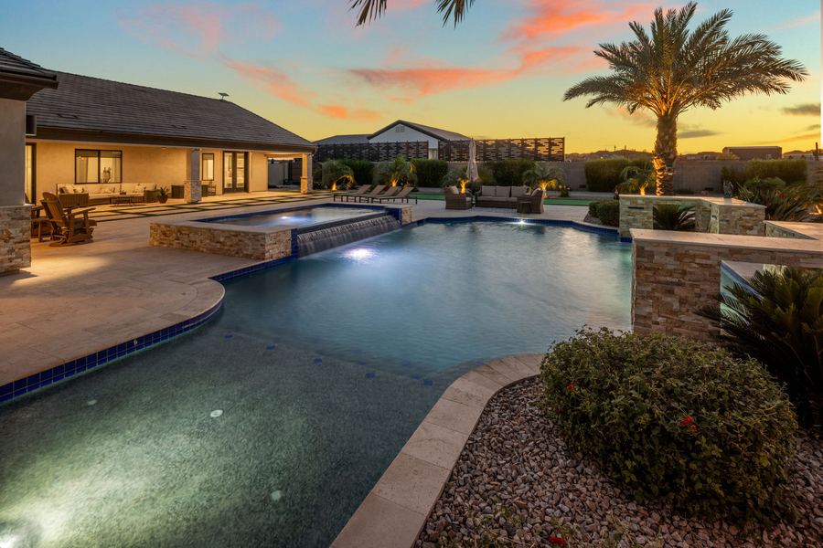 Lit pool curving past desert plantings toward the covered patio at dusk
