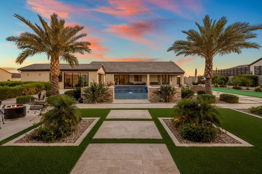 Turf ribbons and travertine pavers leading to the pool and main house at dusk