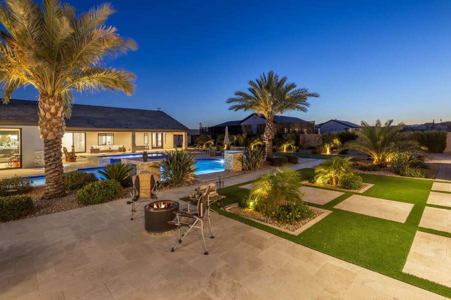Fire pit seating among turf and pavers with lit palms at blue hour