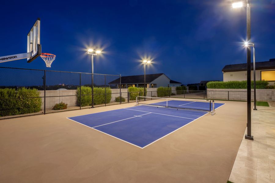 Pickleball court under lights with a basketball hoop at blue hour
