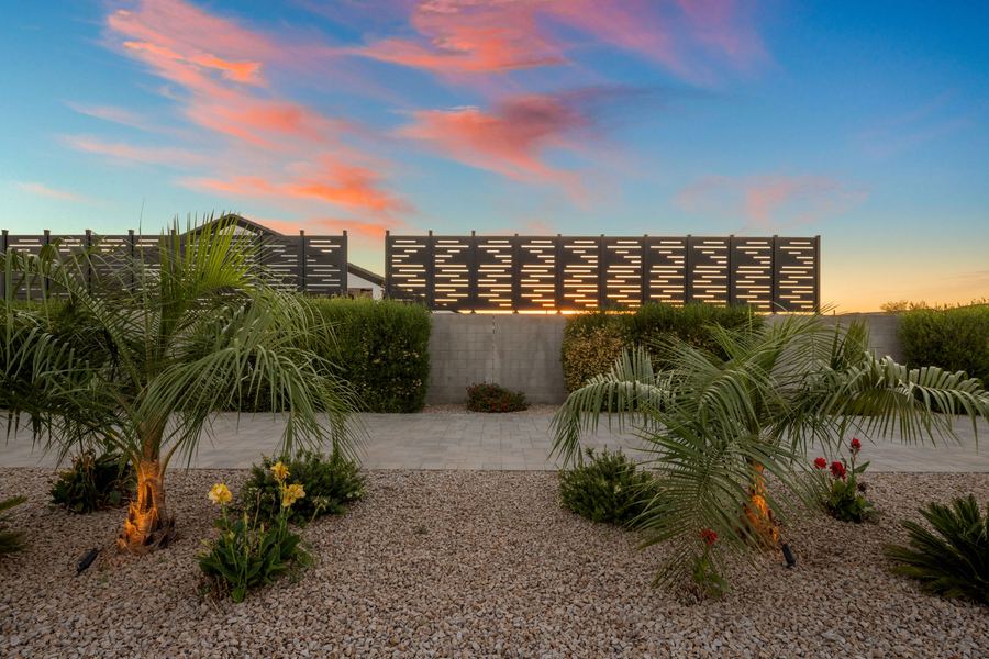 Palms and flowering plants in gravel beds before the privacy screen at sunset