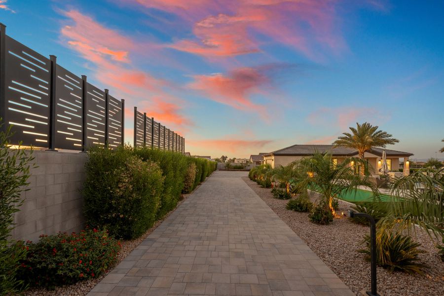 Paver side walk lined with hedges, screen and a landscape light at sunset