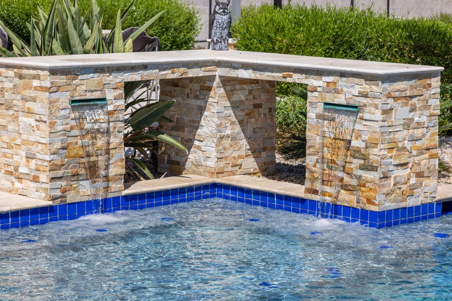 Stacked stone water feature with twin spouts into the pool