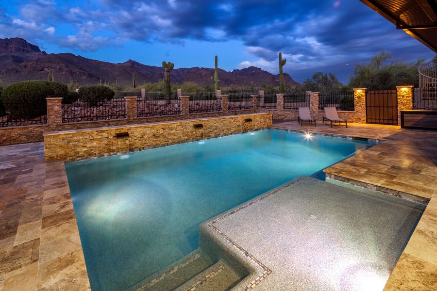 Lit pool with tanning ledge at dusk under a dramatic blue sky