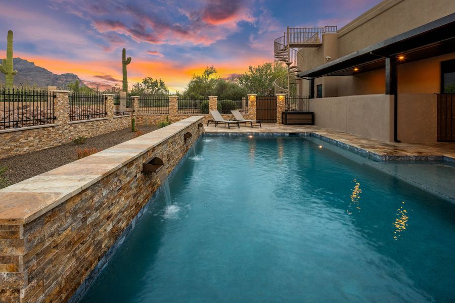 Pool with stacked stone sheer water wall at sunset, mountains on the horizon