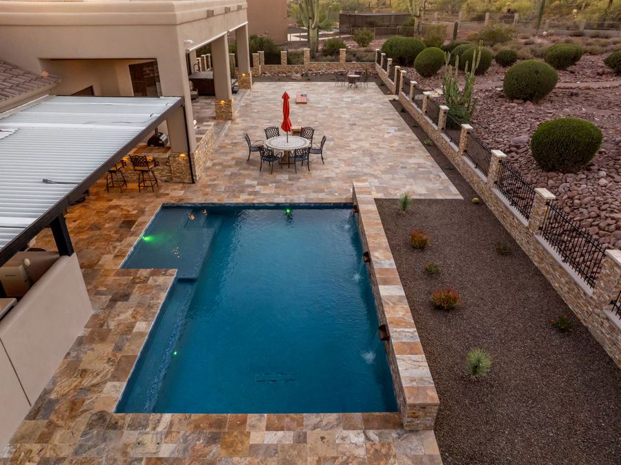 Long rectangular pool and travertine deck seen from above at dusk