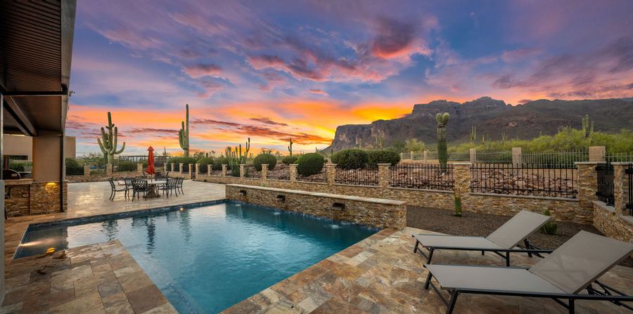 Pool and lounge chairs on travertine at sunset with mountain views