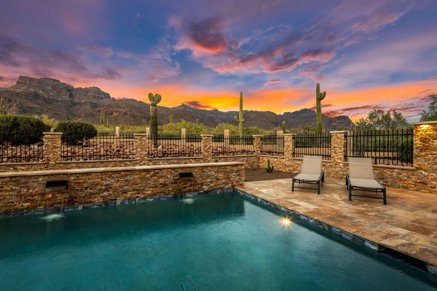 Lit pool beside a stacked stone wall with lounge chairs at sunset