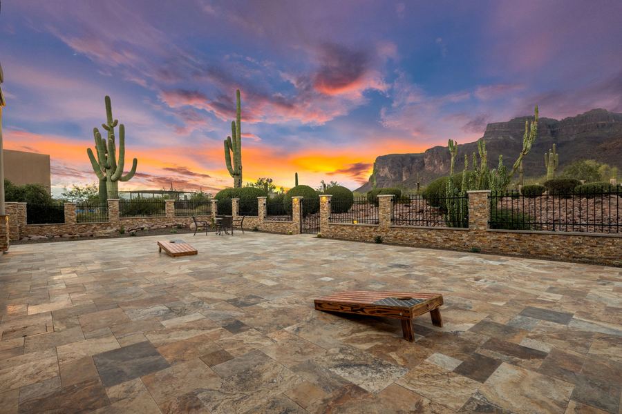 Travertine patio with cornhole set and stone and iron wall at sunset