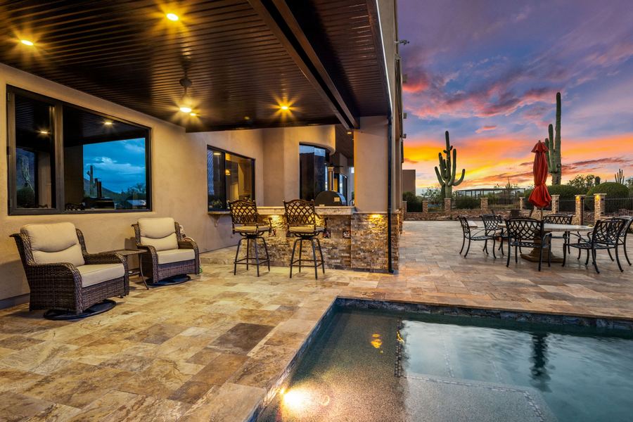 Covered patio with lounge chairs and bar stools beside the pool at dusk