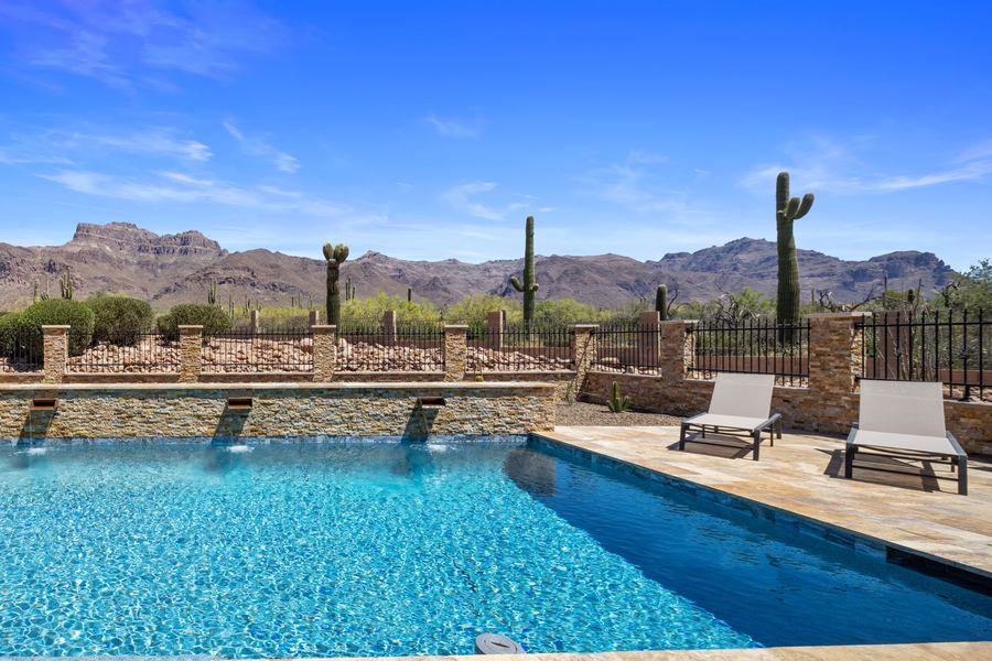 Pool and raised stacked stone wall with mountains and saguaros by day