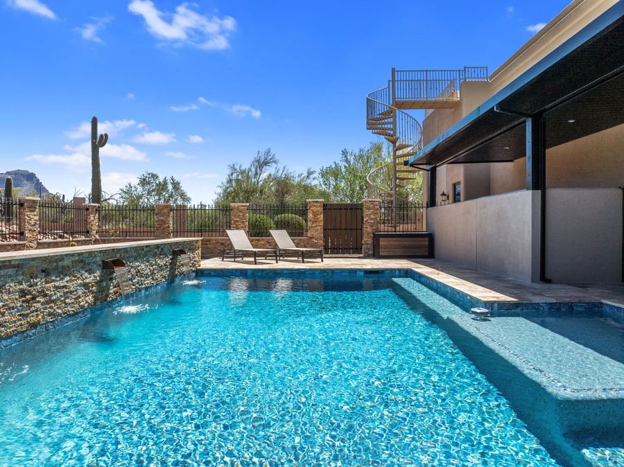 Pool along the house with stone sheer wall on a clear day
