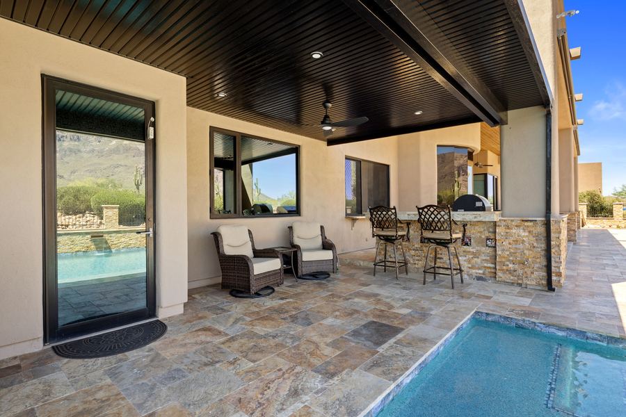 Covered patio with seating, bar stools and a corner of the pool