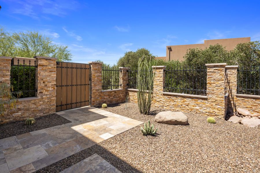Side yard gate set in a stacked stone wall with gravel and boulders
