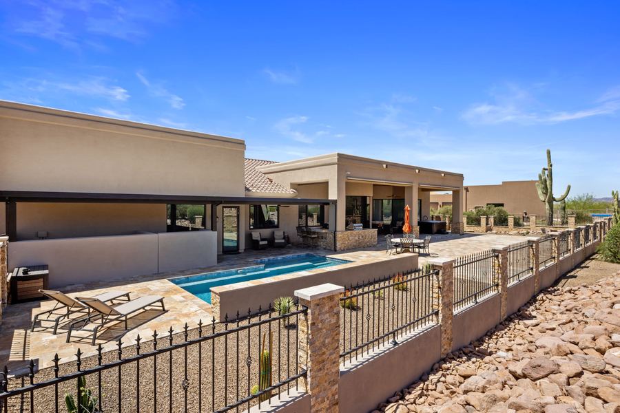 Pool seen past an iron fence with rock lined landscaping