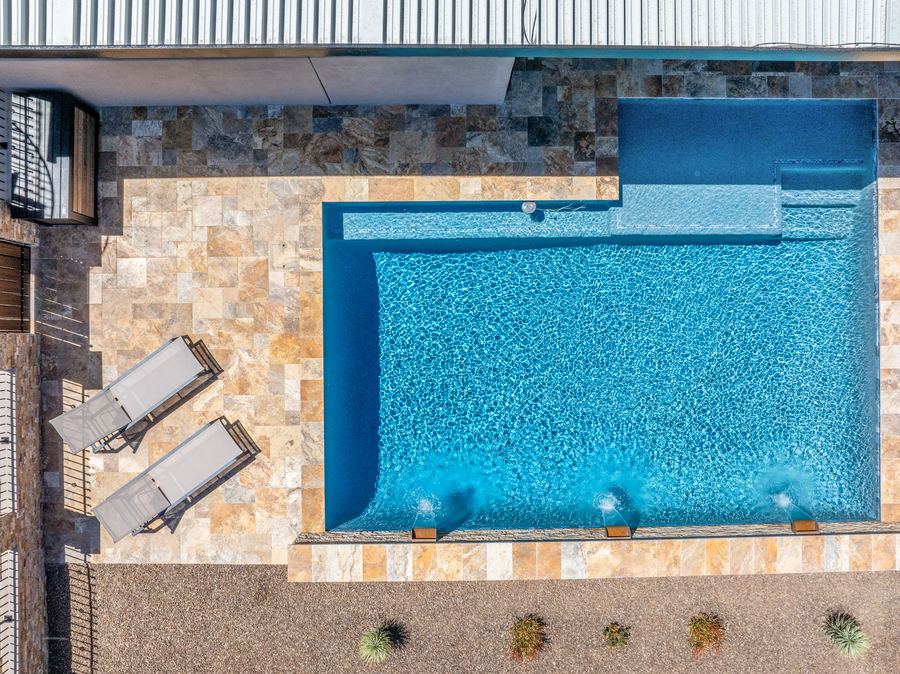 Top down view of the pool and lounge chairs on travertine