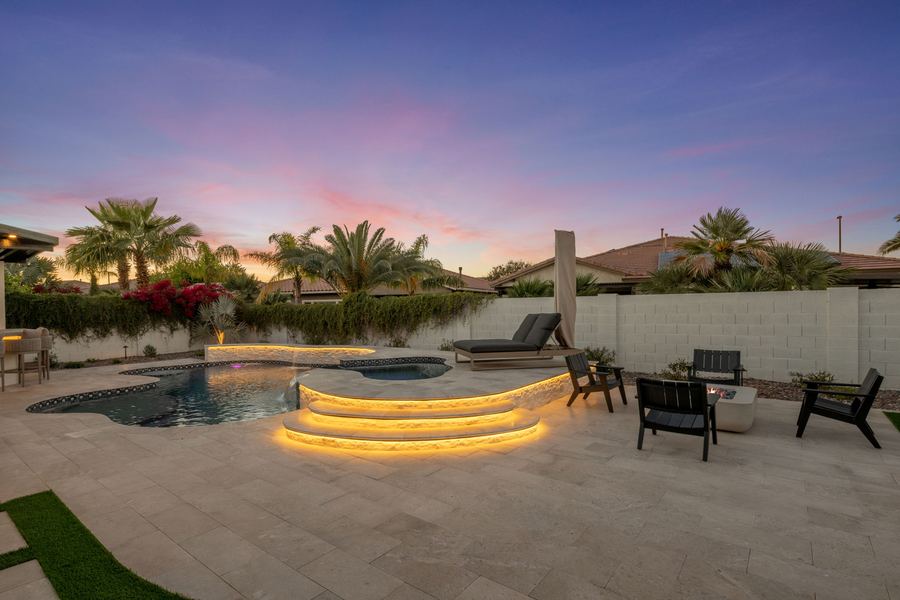 Lit step-down pool entry with fire pit seating beyond at dusk