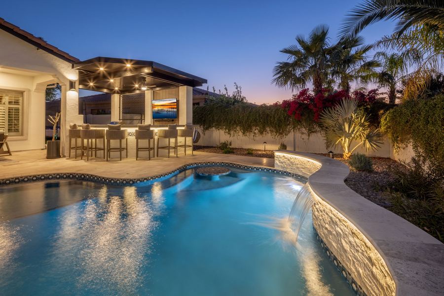 Glowing pool with sheer water features beside the covered bar at night