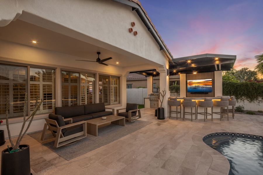 Covered patio lounge and outdoor bar with TV at twilight
