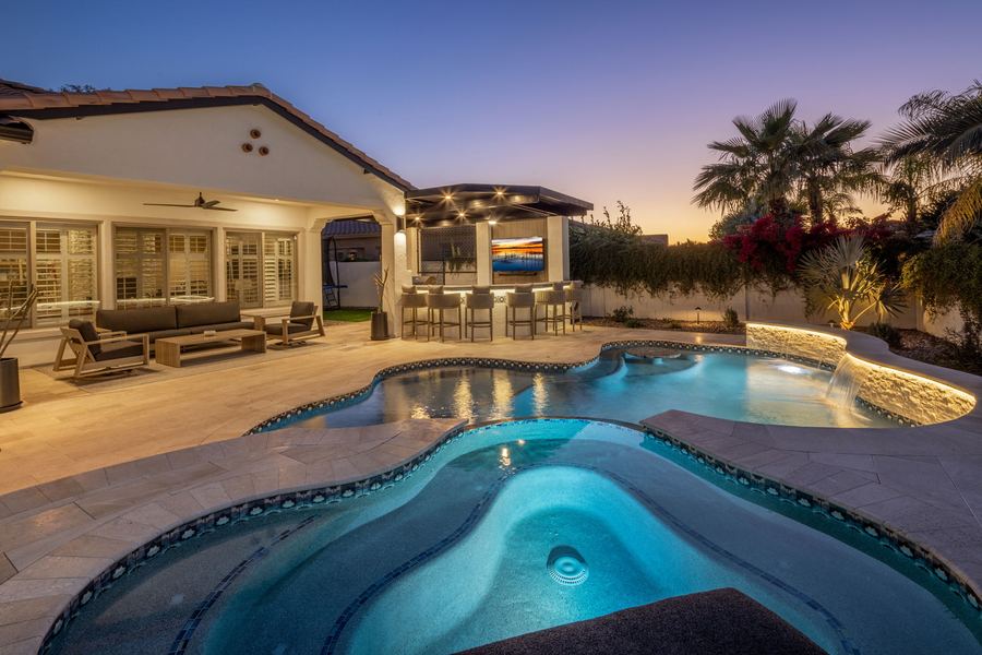 Lit spa and pool in front of the covered patio at dusk