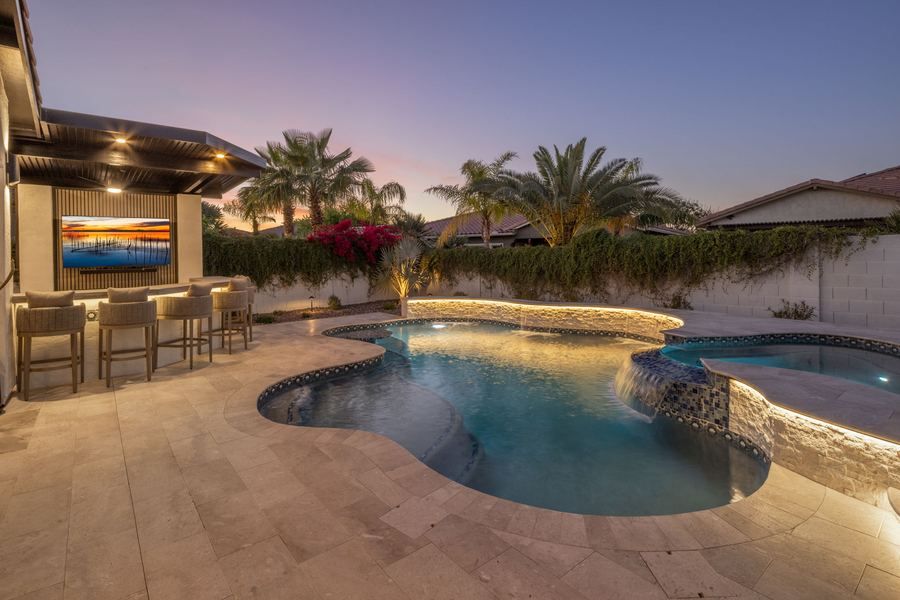 Covered outdoor bar with stools overlooking the freeform pool at dusk