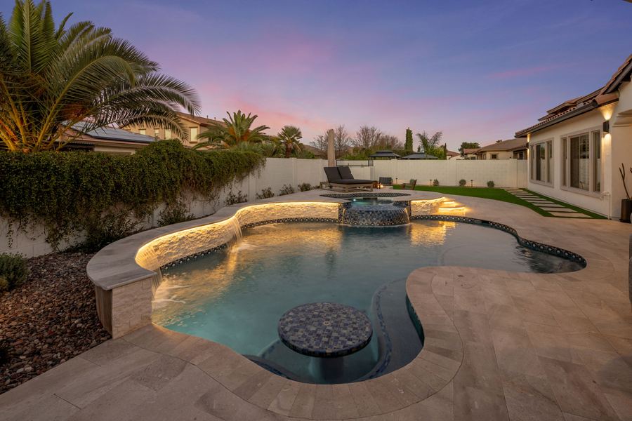 Freeform pool with tiled table and lit raised wall at twilight
