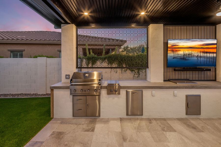 Outdoor kitchen with built-in grill and TV under a covered bar