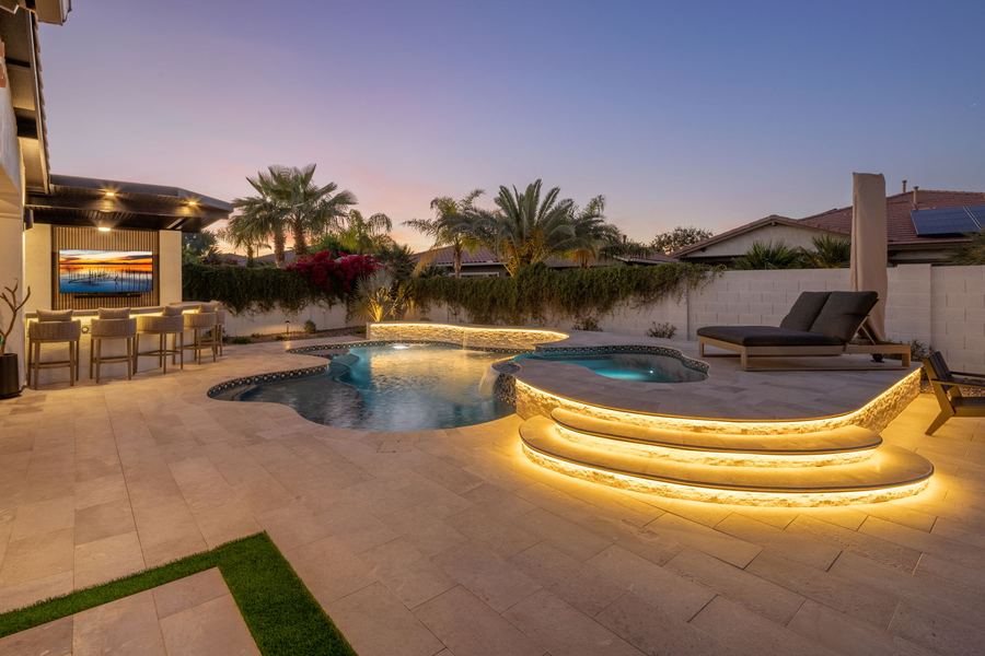 Lit curved pool steps with the spa and covered bar beyond