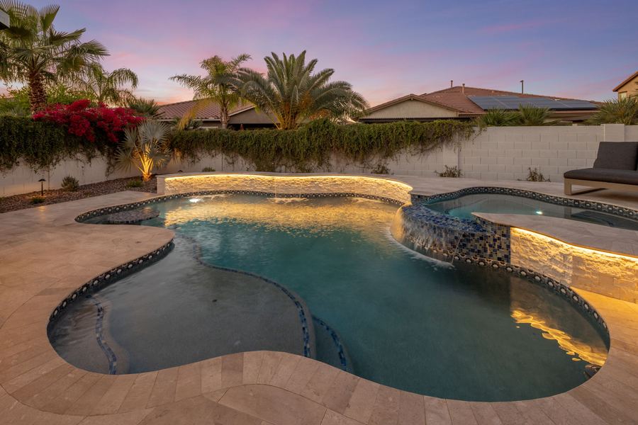 Freeform pool with lit stacked stone wall and raised spa
