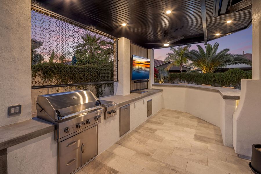 Built-in stainless grill under a covered outdoor kitchen at dusk