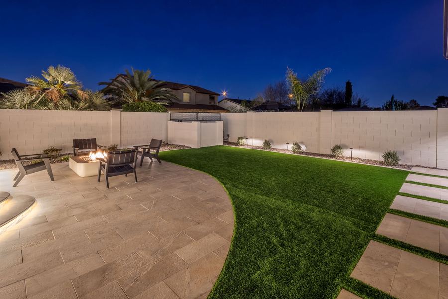 Curved turf lawn and patio with fire pit seating at night