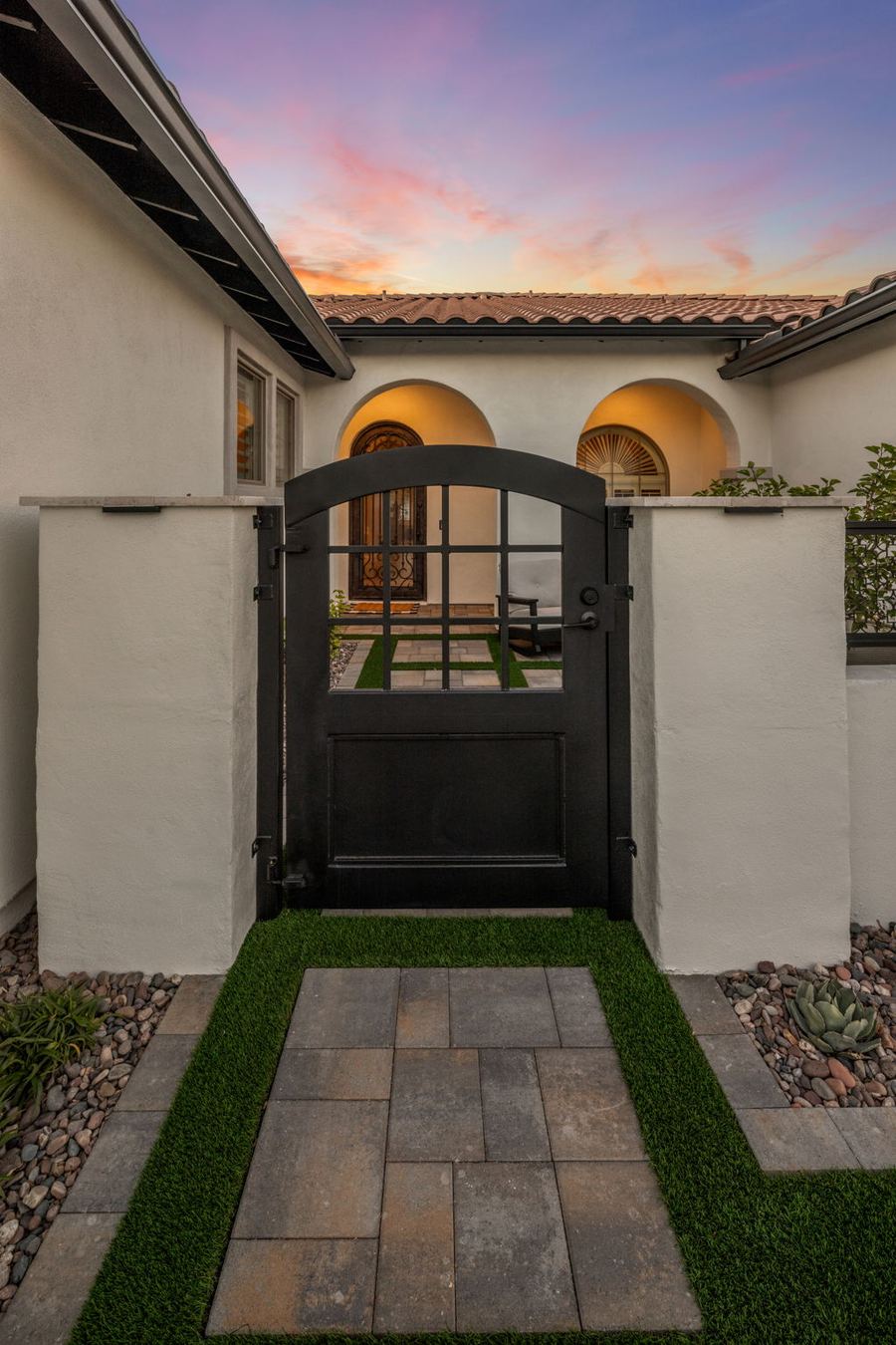 Iron entry gate with paver walkway and turf borders at dusk